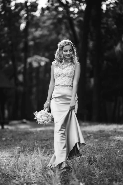 Black and white foto of beautiful bride with a wedding bouquet for a walk in the park. Happy newlywed woman stands among green bushes in the garden. Smiling bride. Wedding day. Fashion bride.