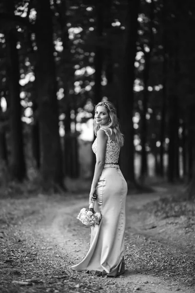 Black and white foto of beautiful bride with a wedding bouquet for a walk in the park. Happy newlywed woman stands among green bushes in the garden. Smiling bride. Wedding day. Fashion bride.