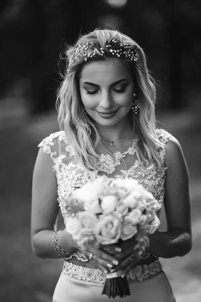 Black and white portrait elegant bride with a wedding bouquet. Beautiful blonde bride stands among green bushes in the garden. Happy newlywed woman. Smiling bride. Wedding day. Fashion bride.