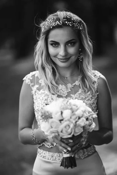 Black and white portrait elegant bride with a wedding bouquet. Beautiful blonde bride stands among green bushes in the garden. Happy newlywed woman. Smiling bride. Wedding day. Fashion bride.