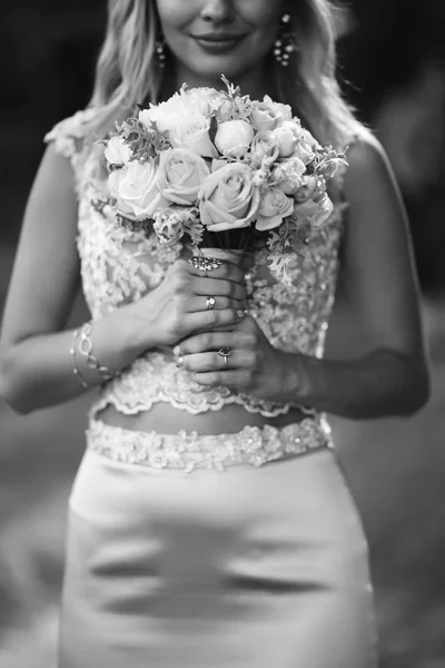 Black and white portrait elegant bride with a wedding bouquet. Beautiful blonde bride stands among green bushes in the garden. Happy newlywed woman. Smiling bride. Wedding day. Fashion bride.