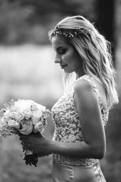 Black and white portrait elegant bride with a wedding bouquet. Beautiful blonde bride stands among green bushes in the garden. Happy newlywed woman. Smiling bride. Wedding day. Fashion bride.