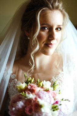 Muhteşem güzel, genç gelin portresi. Gelinin sabahı. Düğün sabahı gelin buketi olan beyaz gelinlik içinde güzel bir gelin. Düğün makyajlı ve saç stili mutlu bir yeni evli kadın.. 