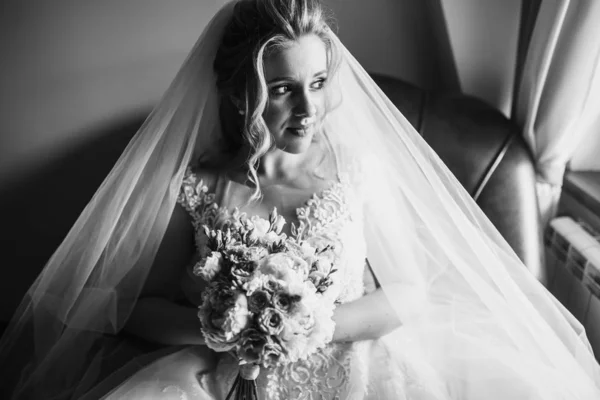 Black and white foto of beautiful bride with wedding flowers bouquet, attractive woman in wedding dress. Happy newlywed woman. Bride with wedding makeup and hairstyle. Morning of the bride.