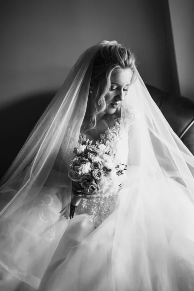 Black and white foto of beautiful bride with wedding flowers bouquet, attractive woman in wedding dress. Happy newlywed woman. Bride with wedding makeup and hairstyle. Morning of the bride.
