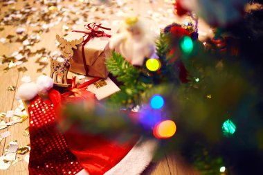 Odadaki köknar ağacının yanında kırmızı kurdeleli güzel Noel hediye kutuları. Işıkların arka planında lüks bir yeni yıl hediyesi. Tahta geyik. Tatil hazırlığı. Yeni yıl konsepti.