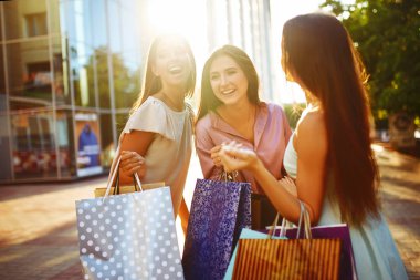 Güzel bir yaz günü. Alışveriş yaptıktan sonra şehirde dolaşan güzel kızlar. Üç kadın renkli alışveriş torbalarıyla el ele tutuşuyor. Tüketim, alımlar, satışlar, yaşam tarzı.