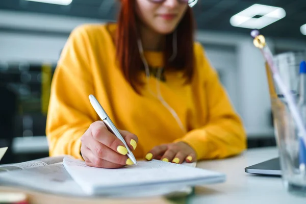 A young woman\'s hand is writing in daily planner. Freelancer works and makes notes.Teenager student in a yellow sweater prepares for exams. Startup small business.