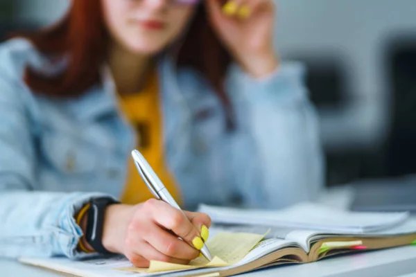 Young woman's hands holding pen and writing in daily planner. Teenager student in a yellow sweater prepares for exams. Freelancer works and makes notes. Startup small business.