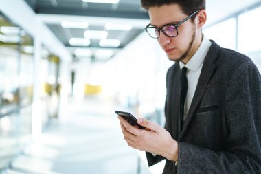 Modern ofiste cep telefonu kullanan bir adamın elleri. İş adamı telefonu elinde tutuyor. Elinde telefon olan takım elbiseli şık bir adam telefonda bir mesaj yazdırıyor.. 