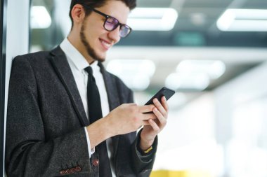 Modern ofiste cep telefonu kullanan bir adamın elleri. İş adamı telefonu elinde tutuyor. Elinde telefon olan takım elbiseli şık bir adam telefonda bir mesaj yazdırıyor.. 