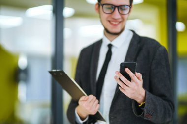Modern ofiste cep telefonu kullanan bir adamın elleri. İş adamı telefonu elinde tutuyor. Elinde telefon olan takım elbiseli şık bir adam telefonda bir mesaj yazdırıyor.. 