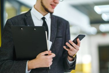 Modern ofiste cep telefonu kullanan bir adamın elleri. İş adamı telefonu elinde tutuyor. Elinde telefon olan takım elbiseli şık bir adam telefonda bir mesaj yazdırıyor.. 