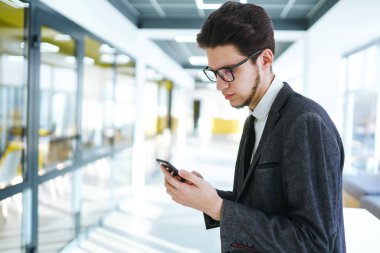 Gözlüklü genç ofis çalışanı cep telefonu kullanıyor. İş adamı telefonu elinde tutuyor. Elinde telefon olan takım elbiseli şık bir adam telefonda mesaj bırakıyor. İletişim konsepti.