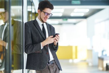 Gözlüklü genç ofis çalışanı cep telefonu kullanıyor. İş adamı telefonu elinde tutuyor. Elinde telefon olan takım elbiseli şık bir adam telefonda mesaj bırakıyor. İletişim konsepti.