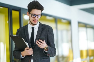 Gözlüklü genç ofis çalışanı cep telefonu kullanıyor. İş adamı telefonu elinde tutuyor. Elinde telefon olan takım elbiseli şık bir adam telefonda mesaj bırakıyor. İletişim konsepti.
