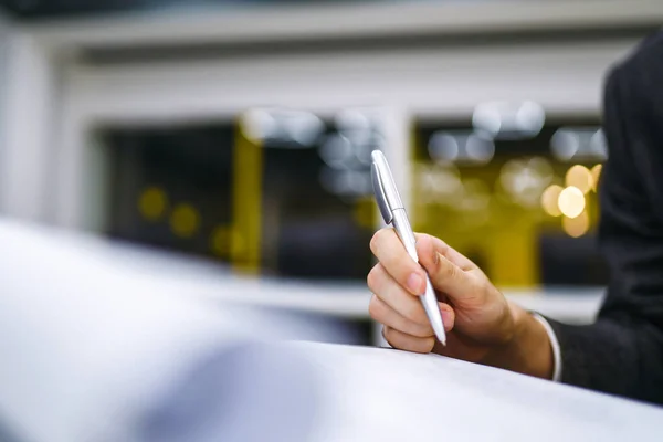 Pen in office worker hand. Close up of the hands of a businessman in a suit signing or writing a document on a sheet of white paper using a pen. Working online concept, business concept.