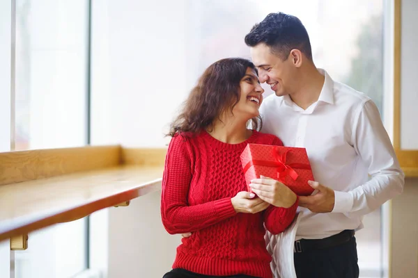 Cheerful couple with gift in hands enjoying together on Christmas eve. Winter holidays. A young loving couple celebrating Valentine\'s Day in the restaurant. Lovers give each other gifts.