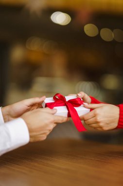 Adam karısına kırmızı kurdeleli bir hediye kutusu veriyor. Erkeğin elleri, kıza sürpriz hediye kutusu verir. Sevgililer birbirlerine hediyeler verir. Sevgililer Günü 'nü kutlayan genç bir çift. Romantik bir gün..