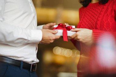 Adam karısına kırmızı kurdeleli bir hediye kutusu veriyor. Erkeğin elleri, kıza sürpriz hediye kutusu verir. Sevgililer birbirlerine hediyeler verir. Sevgililer Günü 'nü kutlayan genç bir çift. Romantik bir gün..