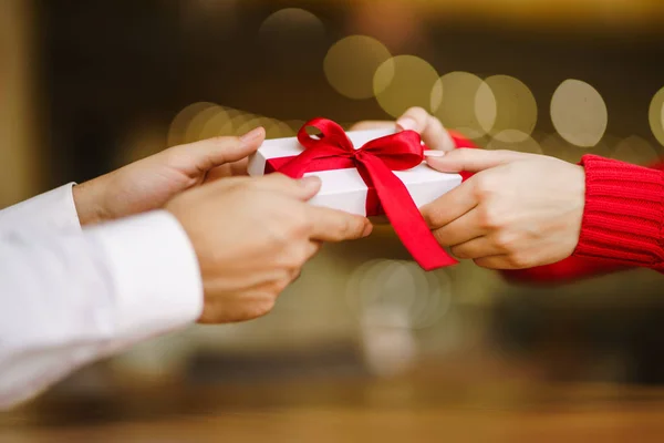 Man gives to his woman a gift box with red ribbon. Hands of man gives surprise gift box for girl. Lovers give each other gifts. Young loving couple celebrating Valentine\'s Day. Romantic day.