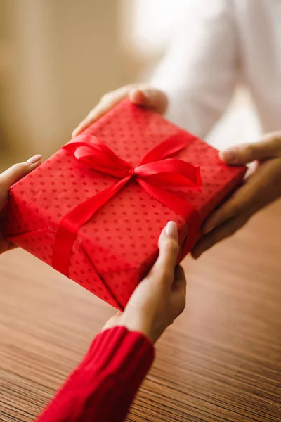 Valentine\'s Day, holiday and surprise concept. Man gives to his woman a red gift box. A loving couple celebrating Valentine\'s Day in the restaurant. Lovers give each other gifts.