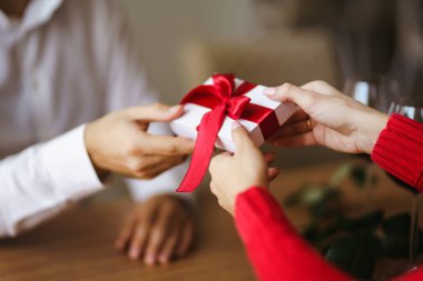 Adam karısına kırmızı kurdeleli bir hediye kutusu veriyor. Erkeğin elleri, kıza sürpriz hediye kutusu verir. Sevgililer Günü 'nü kutlayan genç bir çift. İlişki, sürpriz, doğum günü konsepti.