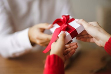 Adam karısına kırmızı kurdeleli bir hediye kutusu veriyor. Erkeğin elleri, kıza sürpriz hediye kutusu verir. Sevgililer Günü 'nü kutlayan genç bir çift. İlişki, sürpriz, doğum günü konsepti.