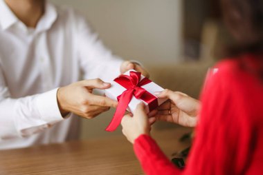 Adam karısına kırmızı kurdeleli bir hediye kutusu veriyor. Erkeğin elleri, kıza sürpriz hediye kutusu verir. Sevgililer Günü 'nü kutlayan genç bir çift. İlişki, sürpriz, doğum günü konsepti.