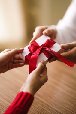 Adam karısına kırmızı kurdeleli bir hediye kutusu veriyor. Erkeğin elleri, kıza sürpriz hediye kutusu verir. Sevgililer Günü 'nü kutlayan genç bir çift. İlişki, sürpriz, doğum günü konsepti.