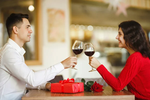 Young couple having a romantic dinner and toasting with cups of red wine. Sweet couple celebrate their anniversary. Valentines day celebration concept. Relationship, surprise and love concept.