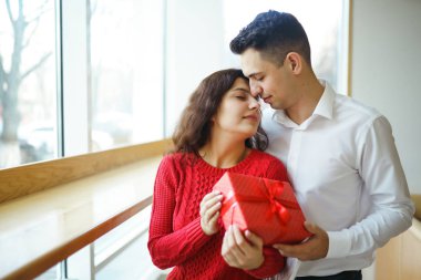 Hediye kucaklaşması olan mutlu çift. Birbirine aşık bir çiftin elinde kırmızı hediye kutusu. Sevgililer Günü, tatil ve sürpriz konsept. Sevgililer birbirlerine hediyeler verir. İlişki ve aşk kavramı.