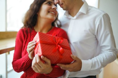 Hediye kucaklaşması olan mutlu çift. Birbirine aşık bir çiftin elinde kırmızı hediye kutusu. Sevgililer Günü, tatil ve sürpriz konsept. Sevgililer birbirlerine hediyeler verir. İlişki ve aşk kavramı.