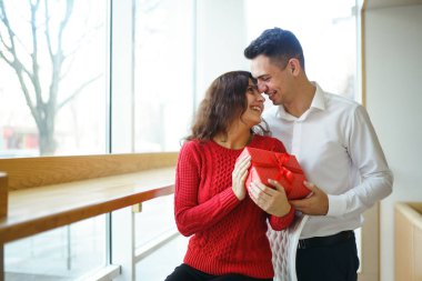 Hediye kucaklaşması olan mutlu çift. Birbirine aşık bir çiftin elinde kırmızı hediye kutusu. Sevgililer Günü, tatil ve sürpriz konsept. Sevgililer birbirlerine hediyeler verir. İlişki ve aşk kavramı.