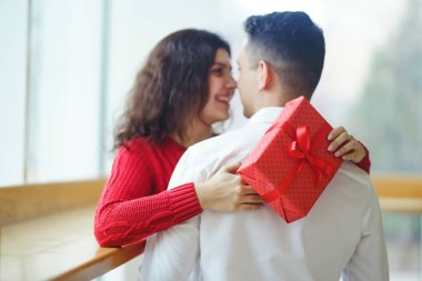 Hediye kucaklaşması olan mutlu çift. Birbirine aşık bir çiftin elinde kırmızı hediye kutusu. Sevgililer Günü, tatil ve sürpriz konsept. Sevgililer birbirlerine hediyeler verir. İlişki ve aşk kavramı.