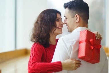 Hediye kucaklaşması olan mutlu çift. Birbirine aşık bir çiftin elinde kırmızı hediye kutusu. Sevgililer Günü, tatil ve sürpriz konsept. Sevgililer birbirlerine hediyeler verir. İlişki ve aşk kavramı.