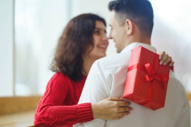 Hediye kucaklaşması olan mutlu çift. Birbirine aşık bir çiftin elinde kırmızı hediye kutusu. Sevgililer Günü, tatil ve sürpriz konsept. Sevgililer birbirlerine hediyeler verir. İlişki ve aşk kavramı.