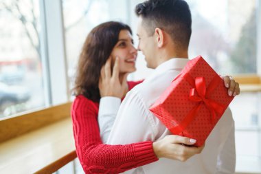 Hediye kucaklaşması olan mutlu çift. Birbirine aşık bir çiftin elinde kırmızı hediye kutusu. Sevgililer Günü, tatil ve sürpriz konsept. Sevgililer birbirlerine hediyeler verir. İlişki ve aşk kavramı.