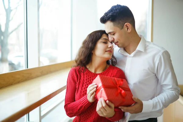 Hediye kucaklaşması olan mutlu çift. Birbirine aşık bir çiftin elinde kırmızı hediye kutusu. Sevgililer Günü, tatil ve sürpriz konsept. Sevgililer birbirlerine hediyeler verir. İlişki ve aşk kavramı.