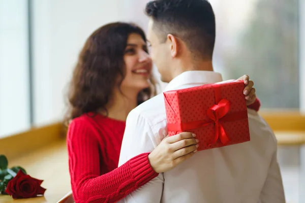 Happy couple with gift hugging. Red gift box in the hands of a couple in love. Valentine\'s Day, holiday and surprise concept. Lovers give each other presents. Relationship and love concept.