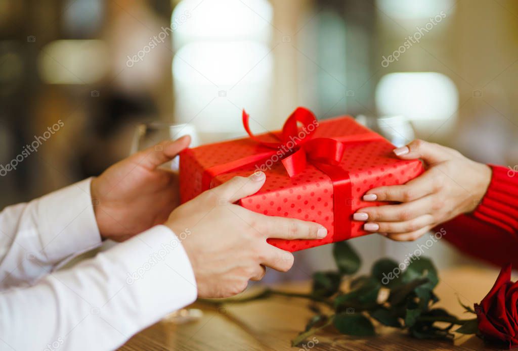 Valentine's Day, holiday and surprise concept. Man gives to his woman a red gift box. Sweet couple celebrate their anniversary. Relationship and love concept.