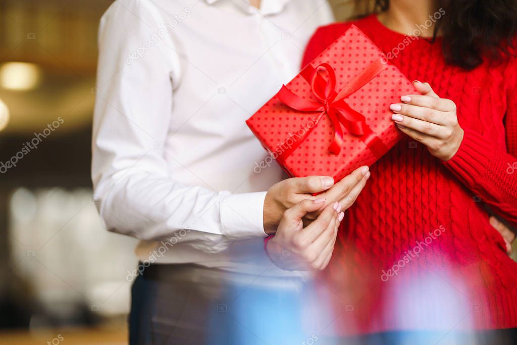 Valentine's Day, holiday and surprise concept. Man gives to his woman a red gift box. Sweet couple celebrate their anniversary. Relationship and love concept.