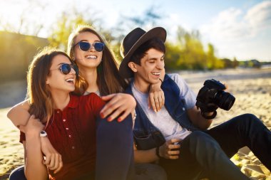 Bir grup mutlu arkadaş sahilde birlikte vakit geçiriyorlar. Genç arkadaşlar gün batımında sahilde eğleniyorlar. Güneş gözlüklü bir grup gülen insan fotoğrafların keyfini çıkarıyor. Yaz, tatil, tatil konsepti 