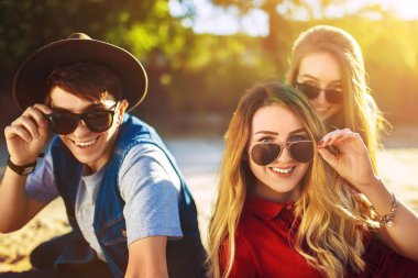 Bir grup mutlu arkadaş sahilde birlikte vakit geçiriyorlar. Genç arkadaşlar gün batımında sahilde eğleniyorlar. Güneş gözlüklü bir grup gülen insan fotoğrafların keyfini çıkarıyor. Yaz, tatil, tatil konsepti 