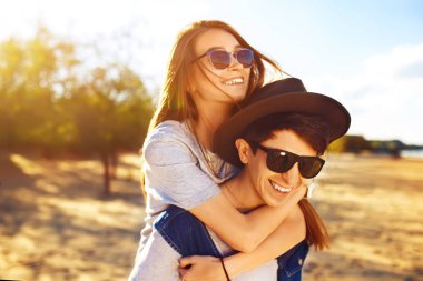 Mutlu genç çift güneşli bir günde sahilde eğleniyor. Sırtında bir kızı taşıyan, gülümseyen ve rahatlayan bir adam. Yaz, tatiller, tatil konsepti. Genç mutlu aşıklar birbirlerinden hoşlanırlar..