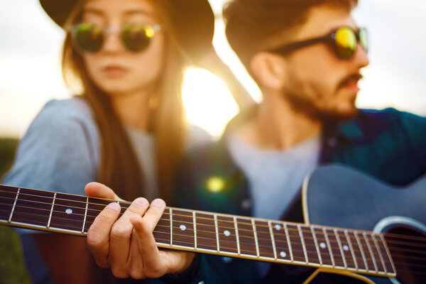 Man playing guitar to his girl on a picnic in park sitting on grass.  Young ouple enjoying party in the summer park. Rest, fun, summer  time together concept.