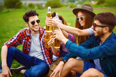 Mutlu arkadaşlar parkta birlikte vakit geçiriyorlar çimenlerde oturup, bira içip sohbet ediyorlar. Bir grup genç yaz parkında eğleniyor. Dinlenme, eğlence, yaz konsepti.