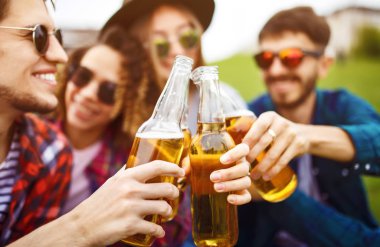 Mutlu arkadaşlar parkta birlikte vakit geçiriyorlar çimenlerde oturup, bira içip sohbet ediyorlar. Bir grup genç yaz parkında eğleniyor. Dinlenme, eğlence, yaz konsepti.