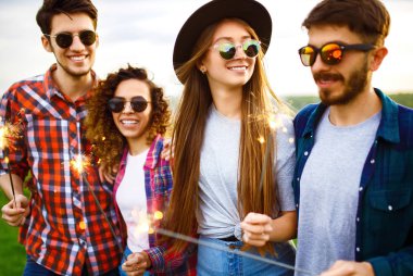 Bir grup arkadaş, yaz parkında çimenlerde oturan maytaplarla eğleniyor. Gençler birlikte eğleniyor. Bir grup genç eğleniyor. Dinlenme, eğlence, yaz, tatil konsepti.