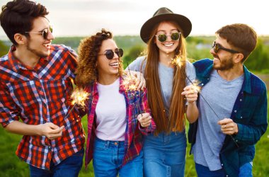 Bir grup arkadaş, yaz parkında çimenlerde oturan maytaplarla eğleniyor. Gençler birlikte eğleniyor. Bir grup genç eğleniyor. Dinlenme, eğlence, yaz, tatil konsepti.